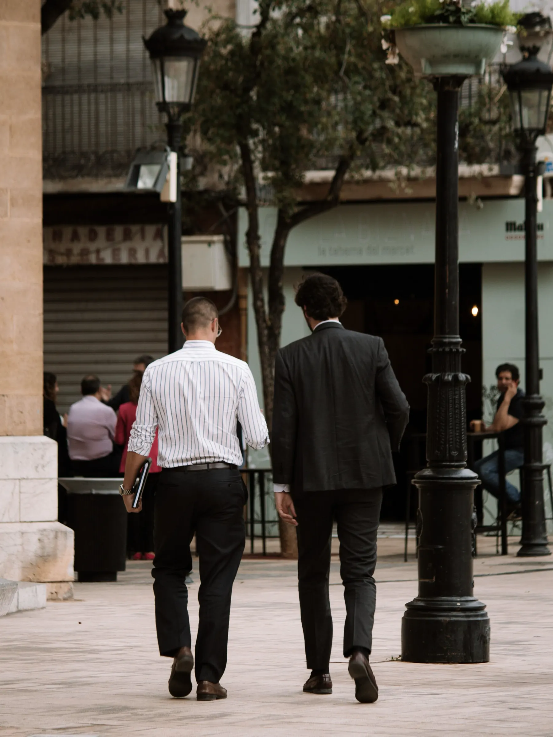 Two men in suits walking together across a Madrid square, seen from behind.