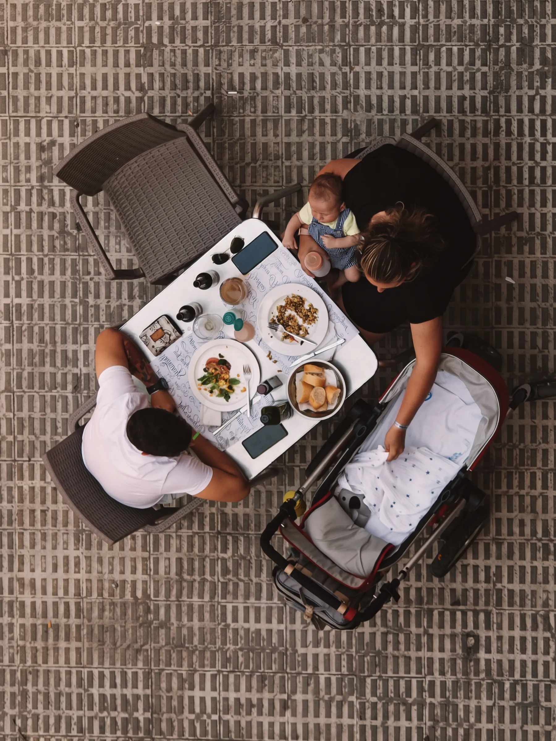 From above: a family at a café table, a baby on a parent's lap and a pram alongside.