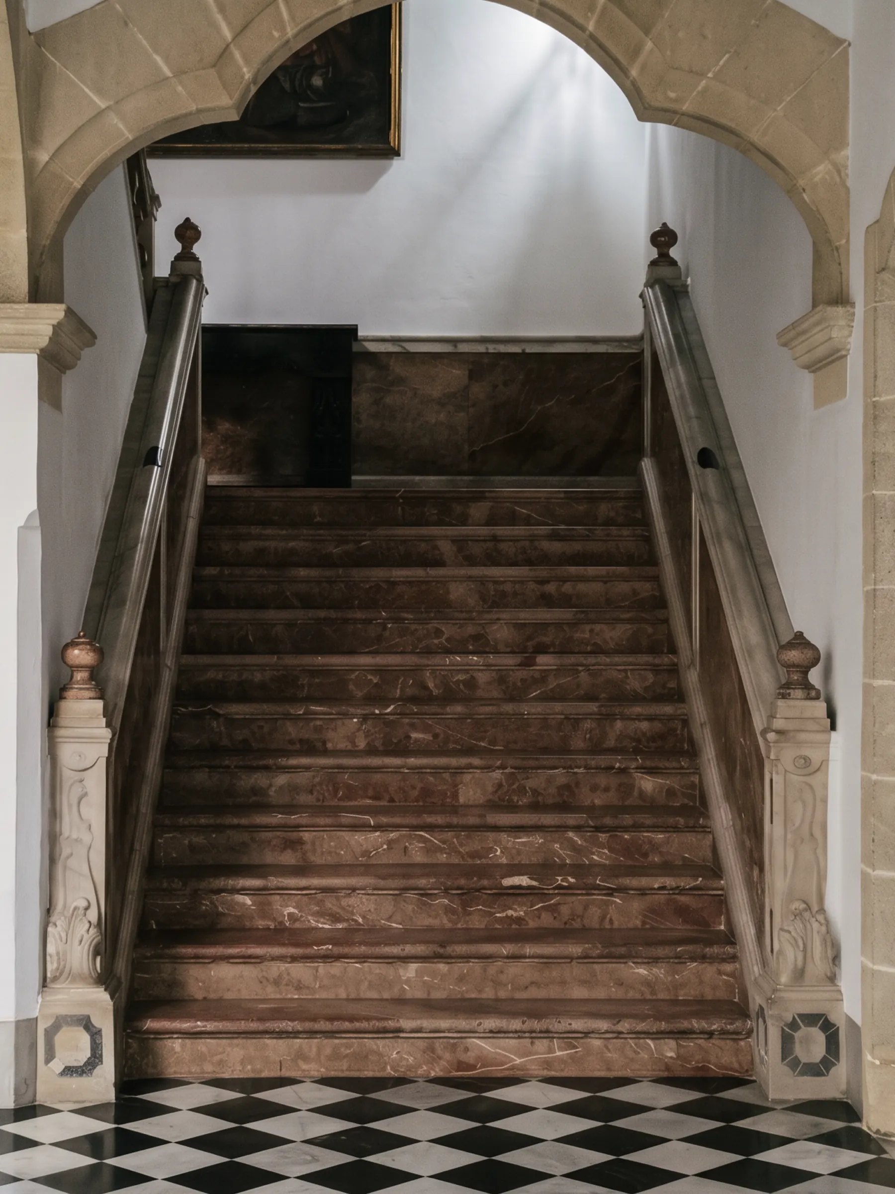 A marble staircase rising beneath a stone arch, checkerboard floor below.
