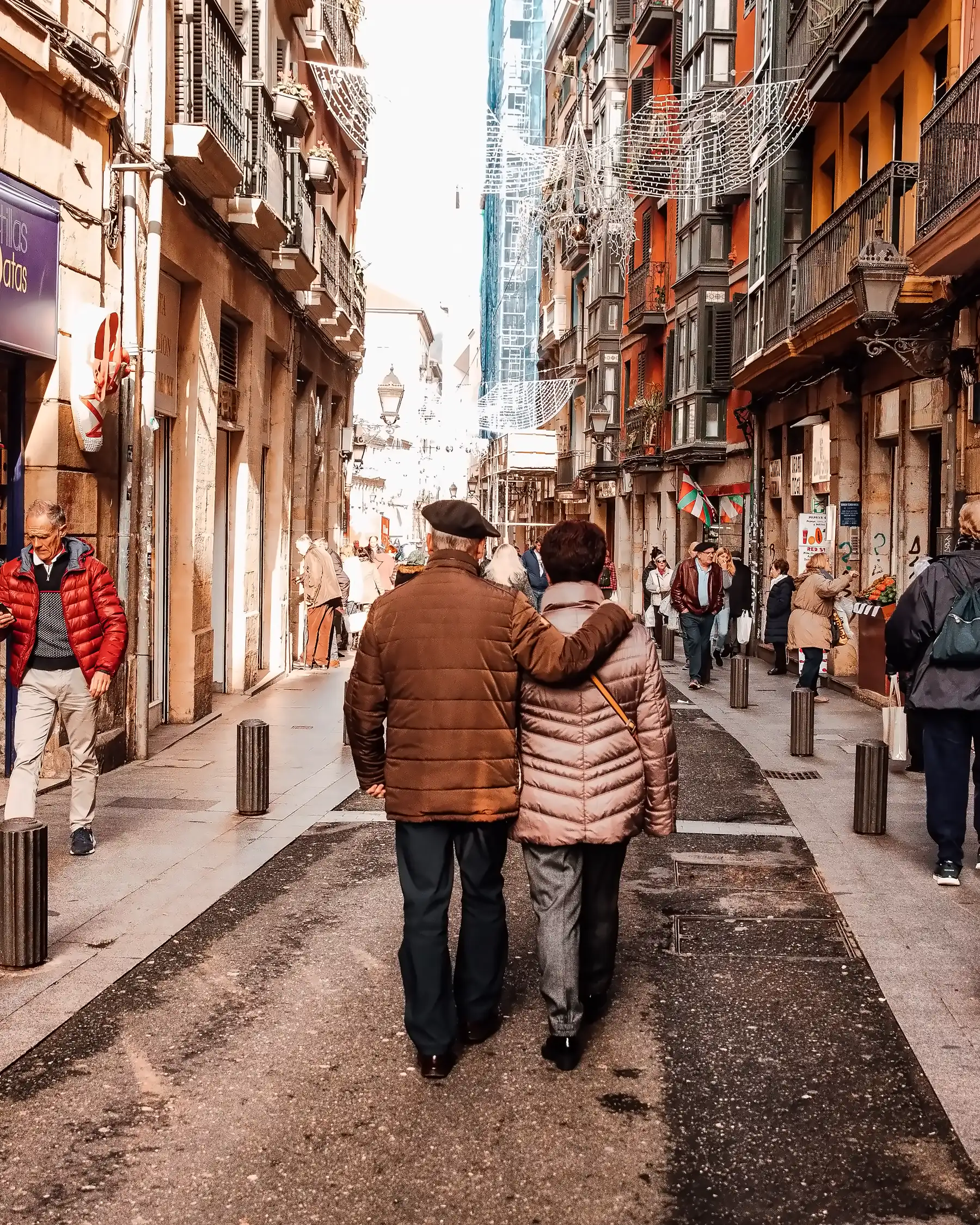 An older couple walking arm in arm down a busy old-town street in northern Spain.