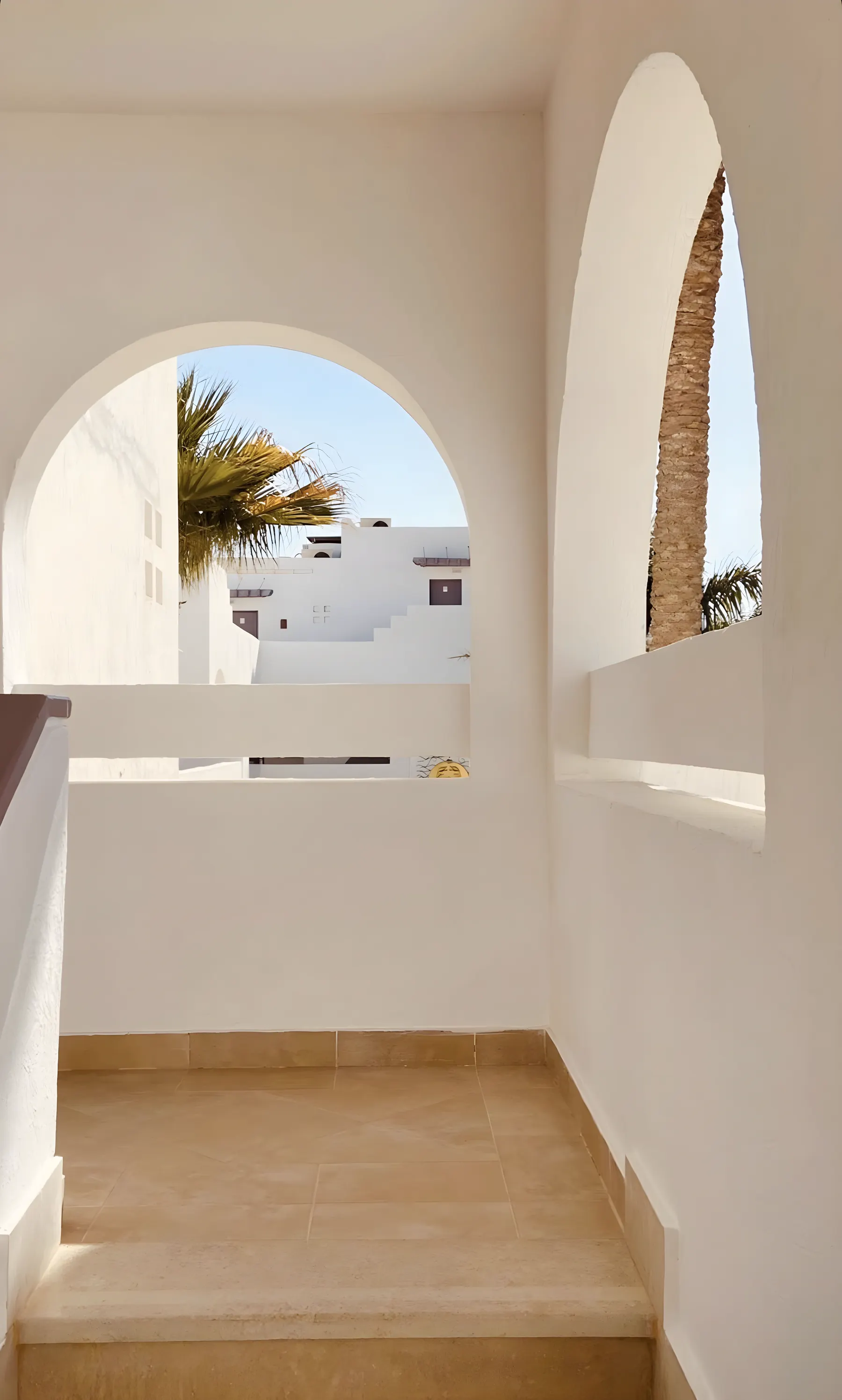 Whitewashed arches on a Mediterranean terrace, palm fronds and white houses in the afternoon light.