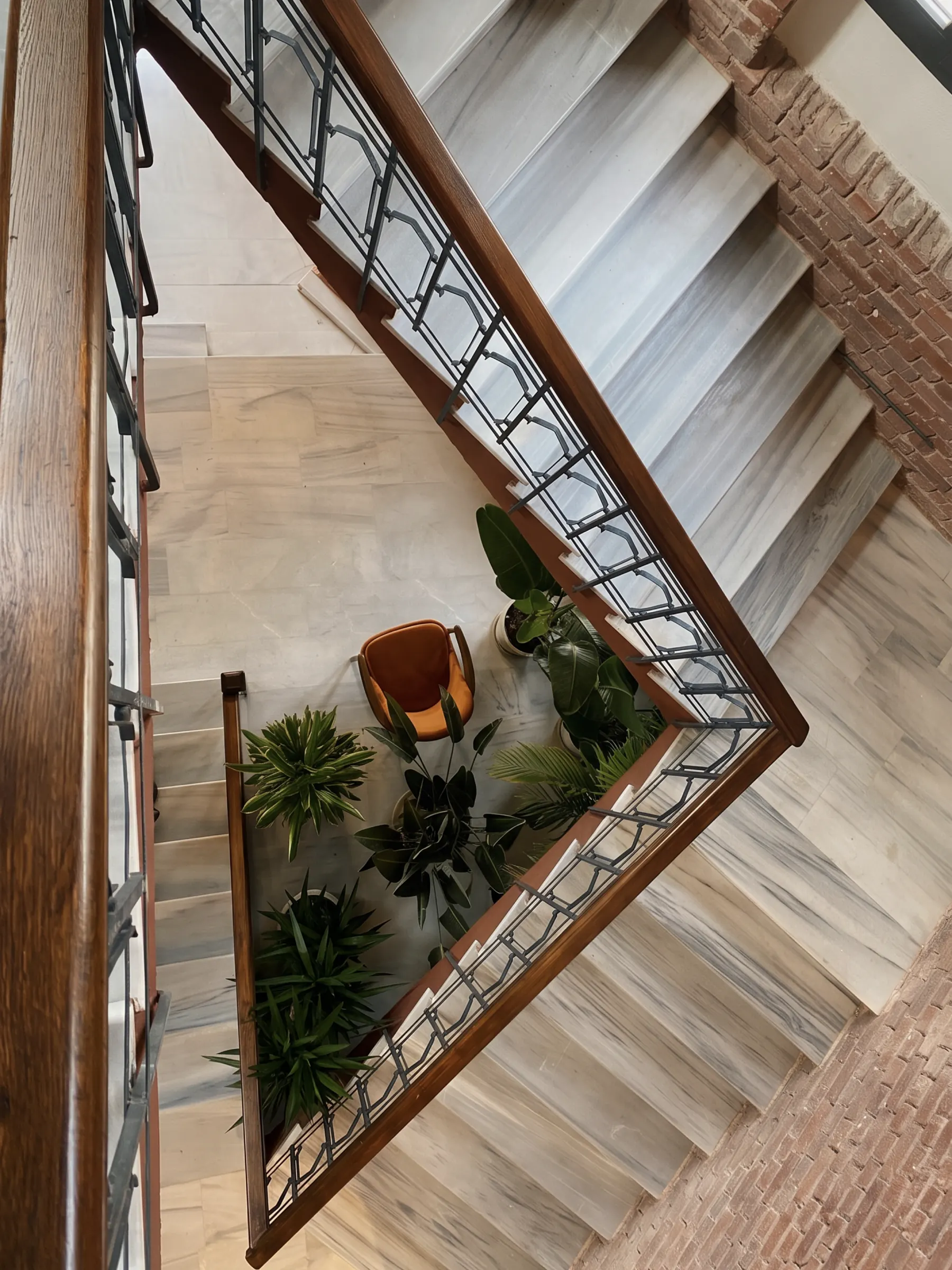 Looking down a marble stairwell with a wrought-iron balustrade and plants on the landing.