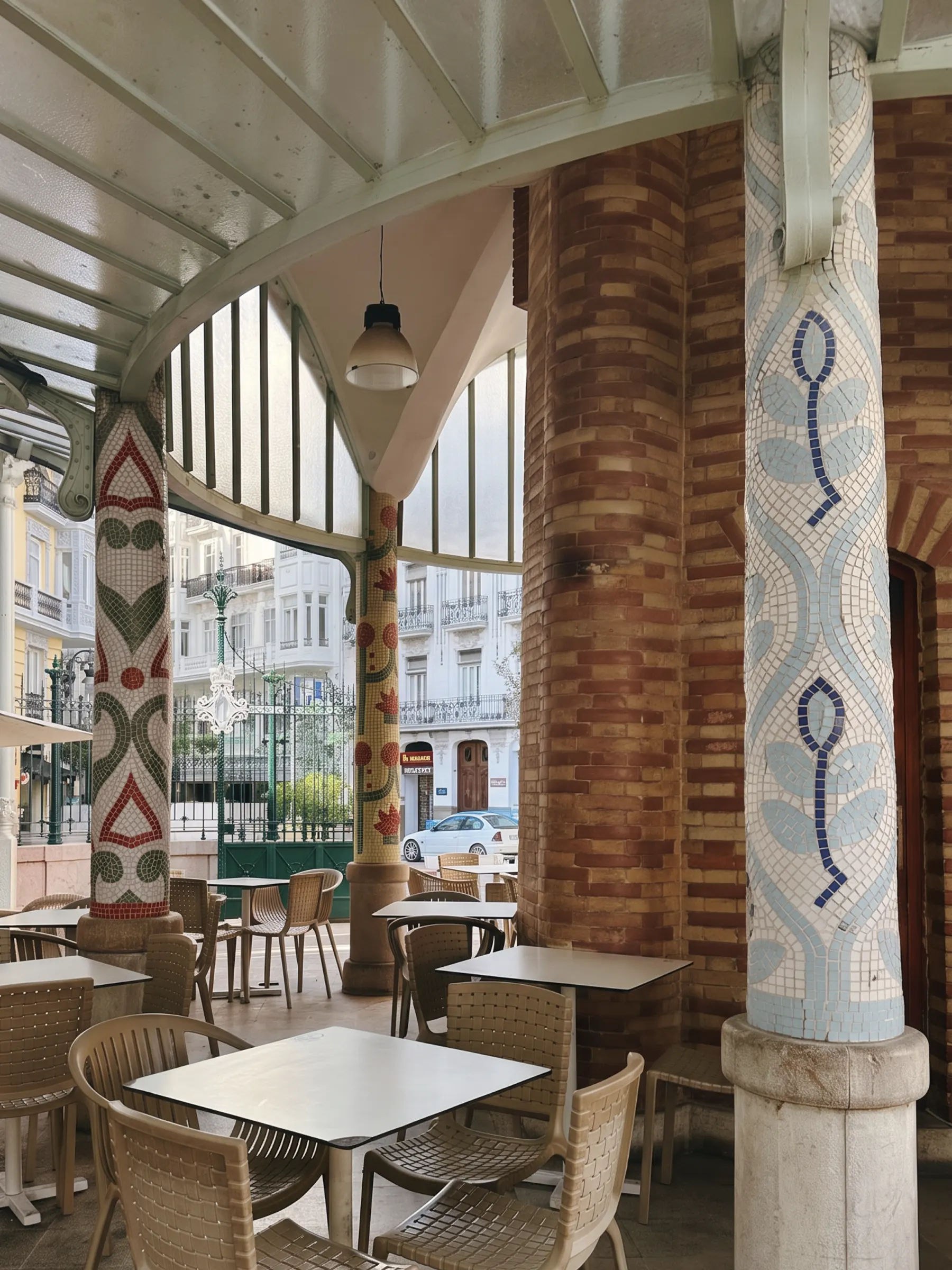 Café tables beneath a Modernista canopy, tiled columns and brick arches opening onto the street.